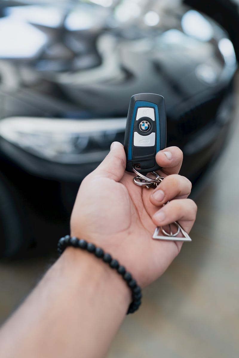 Close-up of a hand holding a luxury car key in focus, with the vehicle blurred in the background.